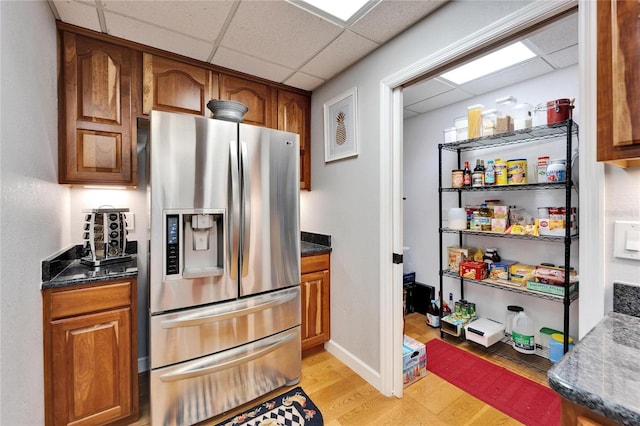 kitchen featuring a drop ceiling, stainless steel refrigerator with ice dispenser, light hardwood / wood-style flooring, and dark stone countertops