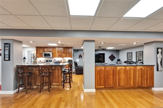 kitchen with kitchen peninsula, light hardwood / wood-style flooring, sink, a paneled ceiling, and a breakfast bar area