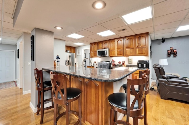 kitchen featuring light hardwood / wood-style flooring, a paneled ceiling, dark stone counters, a breakfast bar area, and stainless steel appliances