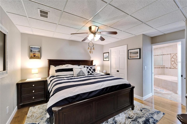 bedroom featuring light hardwood / wood-style floors, a paneled ceiling, ensuite bath, and ceiling fan