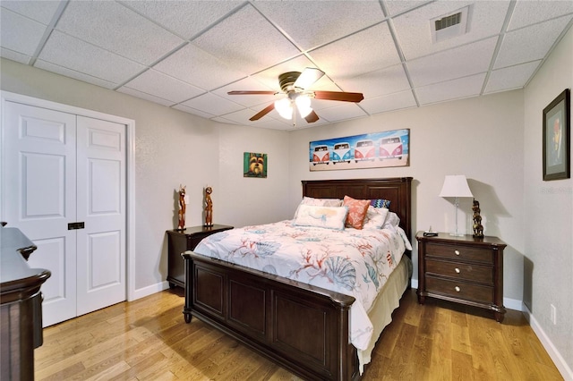 bedroom featuring a closet, ceiling fan, light hardwood / wood-style floors, and a drop ceiling