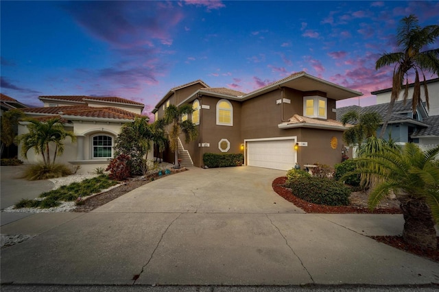 view of front of property featuring driveway, an attached garage, a tile roof, and stucco siding