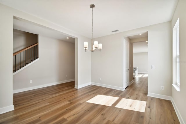 spare room with wood-type flooring and an inviting chandelier