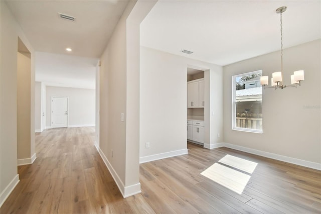 hallway with a notable chandelier and light wood-type flooring