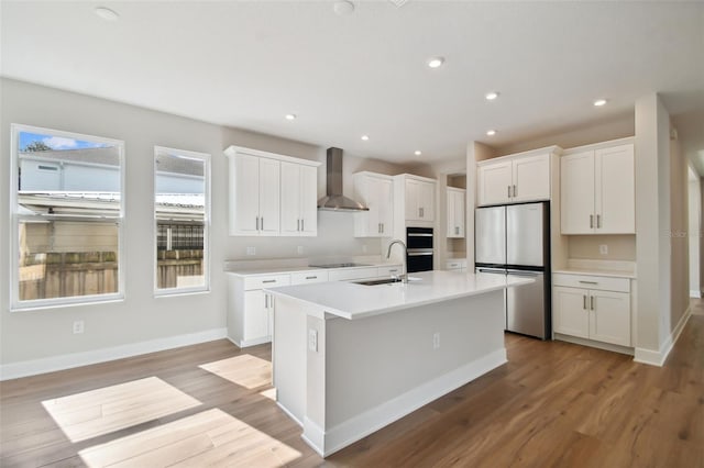 kitchen featuring white cabinetry, wall chimney range hood, stainless steel fridge, and an island with sink