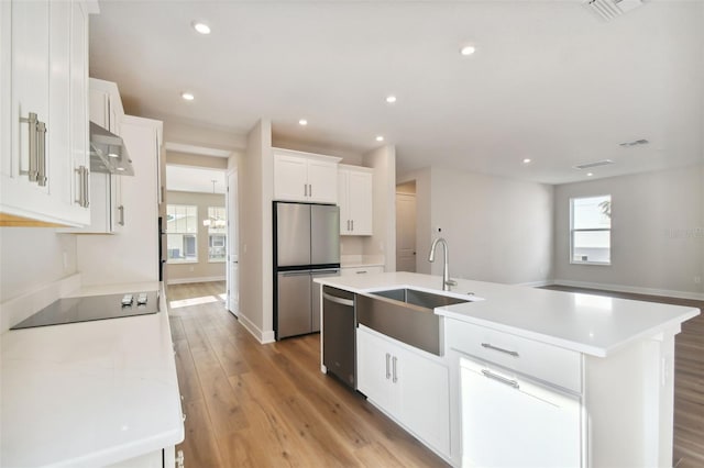 kitchen featuring white cabinetry, stainless steel appliances, sink, light wood-type flooring, and a center island with sink