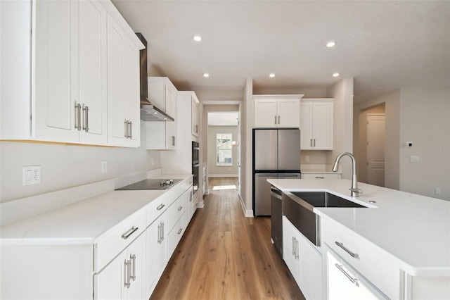 kitchen with white cabinets, wall chimney exhaust hood, stainless steel appliances, sink, and a kitchen island with sink