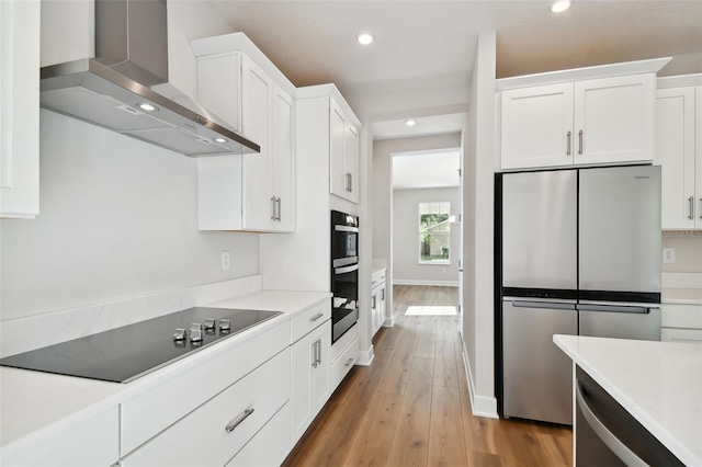 kitchen featuring black appliances, wall chimney range hood, white cabinetry, and light hardwood / wood-style floors