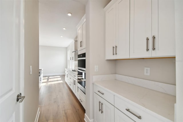 kitchen with light stone countertops, white cabinetry, and light hardwood / wood-style flooring