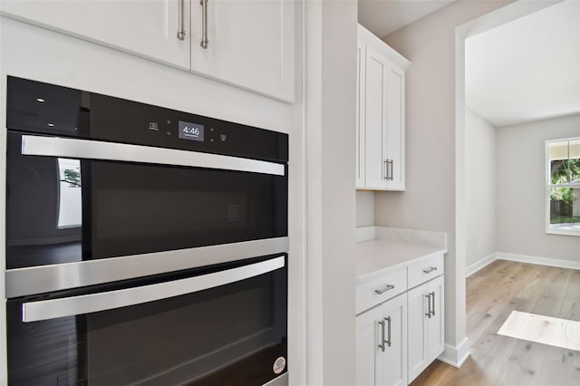 kitchen with light wood-type flooring, white cabinetry, black double oven, and light stone countertops