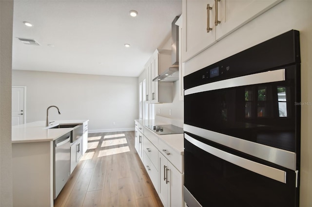 kitchen featuring black appliances, wall chimney exhaust hood, sink, and white cabinetry