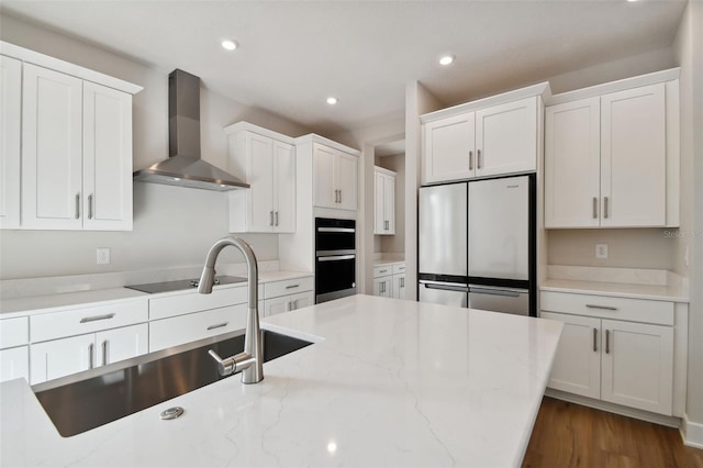 kitchen with dark hardwood / wood-style floors, white cabinetry, light stone countertops, stainless steel fridge, and wall chimney exhaust hood