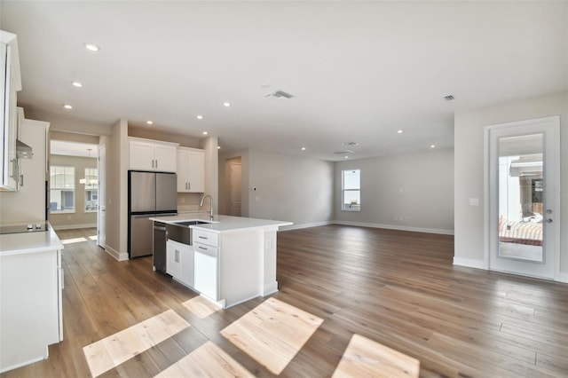 kitchen with light wood-type flooring, sink, white cabinets, and an island with sink