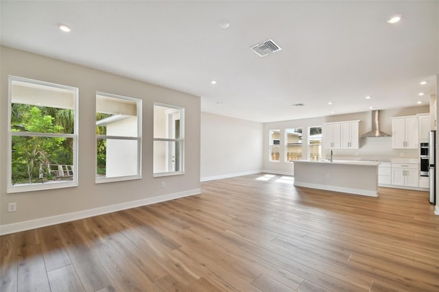 unfurnished living room featuring sink, light wood-type flooring, and a wealth of natural light