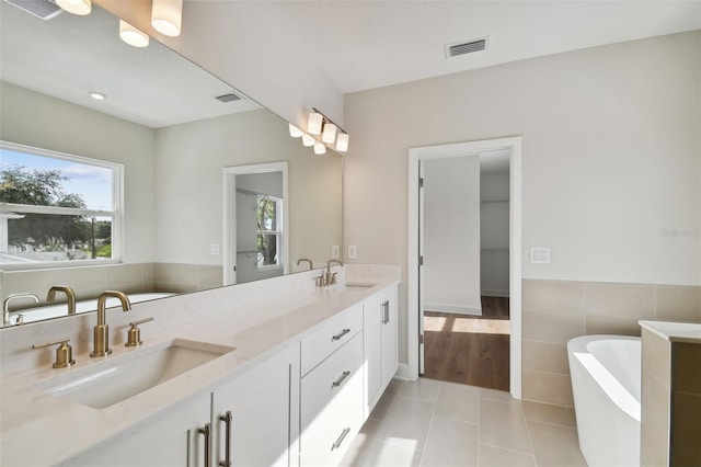 bathroom with vanity, tile patterned flooring, tile walls, and a bath