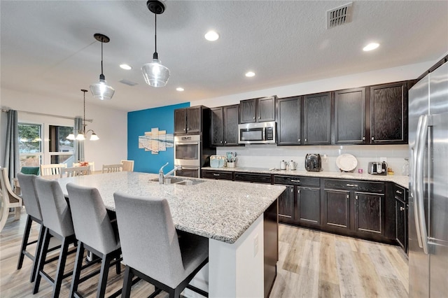 kitchen featuring a kitchen bar, light stone counters, decorative light fixtures, stainless steel appliances, and a kitchen island with sink