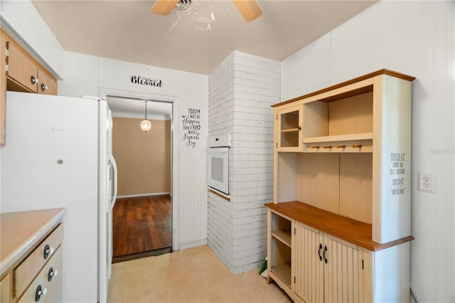 kitchen with ceiling fan, pendant lighting, wooden walls, white appliances, and light brown cabinetry