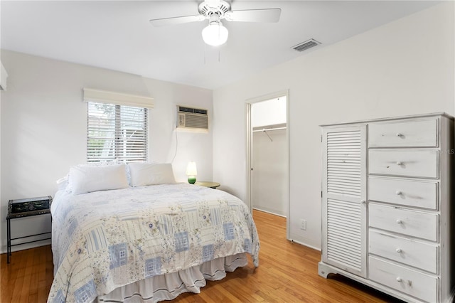 bedroom with ceiling fan, a wall unit AC, light wood-type flooring, a walk in closet, and a closet