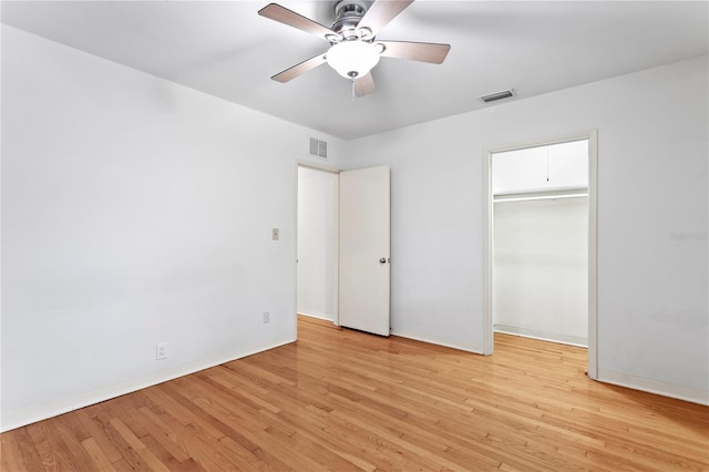 unfurnished bedroom featuring ceiling fan, light hardwood / wood-style floors, a closet, and a walk in closet