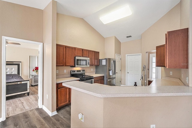 kitchen featuring kitchen peninsula, light hardwood / wood-style flooring, lofted ceiling, and appliances with stainless steel finishes