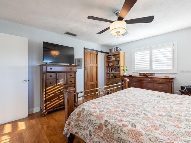 bedroom with ceiling fan, wood-type flooring, a barn door, and a textured ceiling