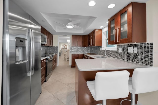 kitchen with a raised ceiling, a breakfast bar, kitchen peninsula, sink, and stainless steel appliances