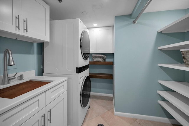 laundry area with stacked washer / dryer, sink, light tile patterned floors, and cabinets