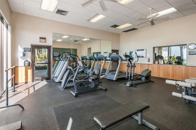 gym with ceiling fan, a drop ceiling, and wood walls