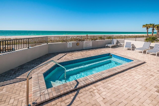 view of swimming pool with a beach view, a water view, and a hot tub