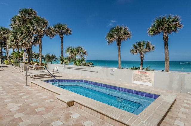 view of pool with a patio area, a community hot tub, a water view, and a view of the beach