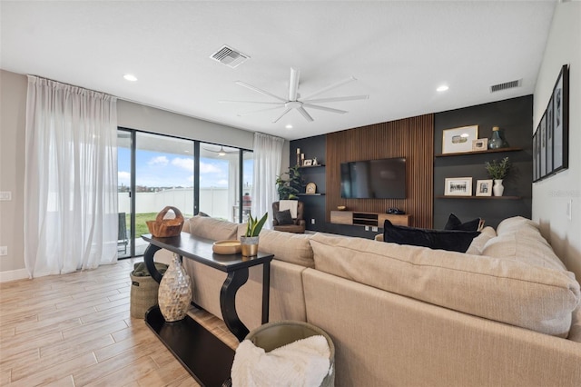 living room with ceiling fan, wooden walls, and light wood-type flooring