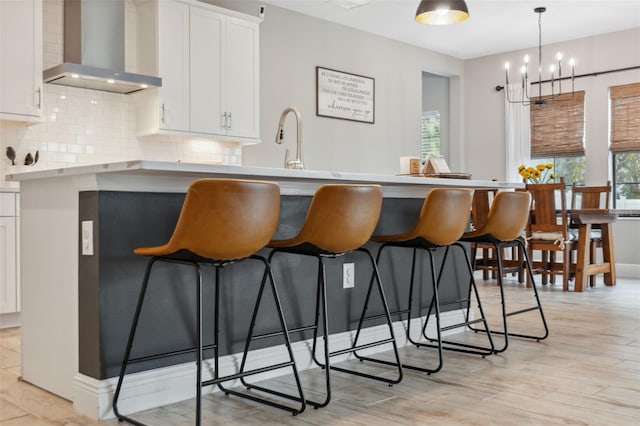 kitchen with tasteful backsplash, white cabinetry, a breakfast bar area, hanging light fixtures, and wall chimney exhaust hood