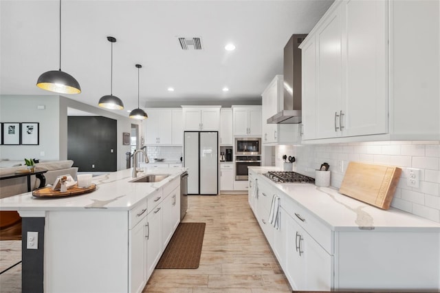 kitchen featuring appliances with stainless steel finishes, pendant lighting, sink, a large island with sink, and wall chimney range hood