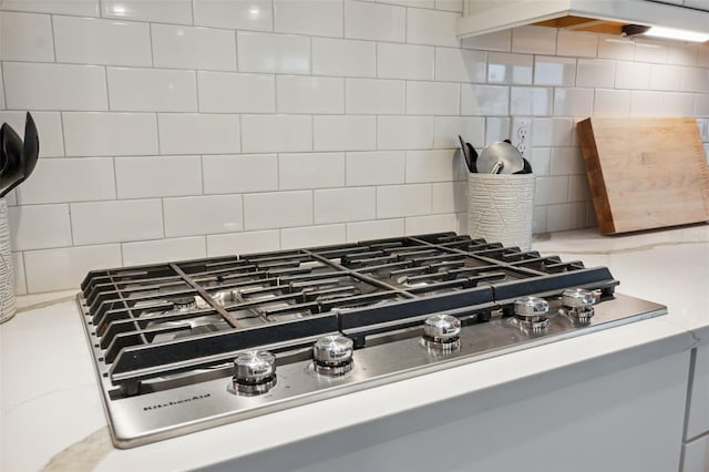 interior details with backsplash, range hood, and stainless steel gas stovetop