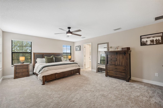 bedroom with ensuite bathroom, light colored carpet, and ceiling fan