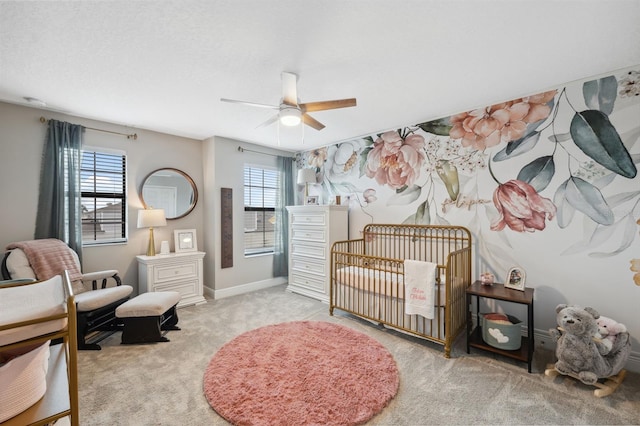 carpeted bedroom featuring a nursery area, ceiling fan, and multiple windows