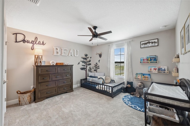 bedroom featuring a crib, light carpet, a textured ceiling, and ceiling fan