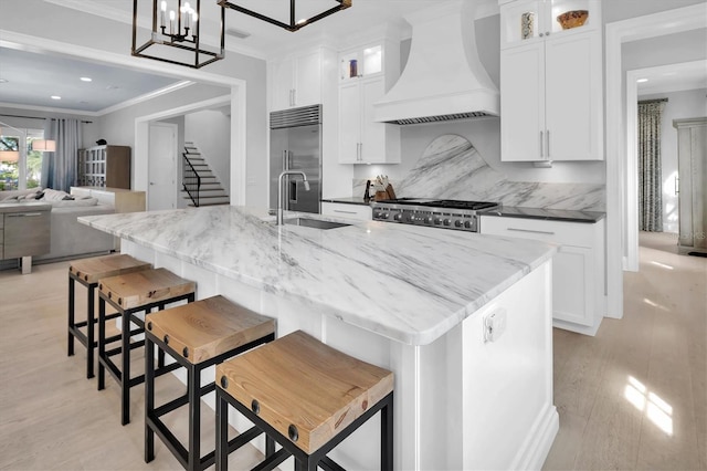 kitchen featuring premium range hood, an island with sink, a kitchen bar, and built in refrigerator