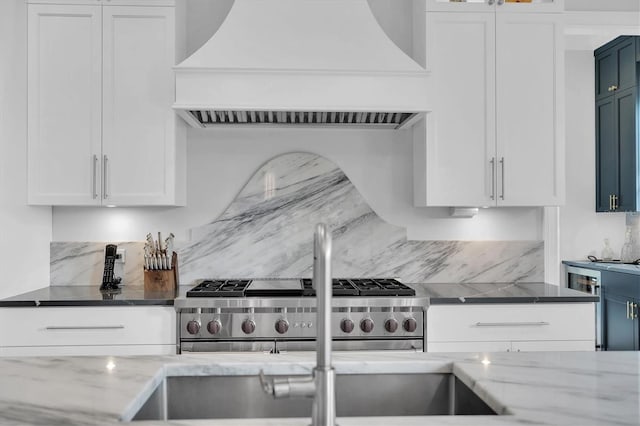 kitchen with blue cabinetry, white cabinetry, custom range hood, backsplash, and light stone counters