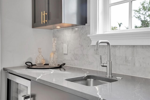 kitchen with tasteful backsplash, gray cabinetry, sink, light stone counters, and beverage cooler