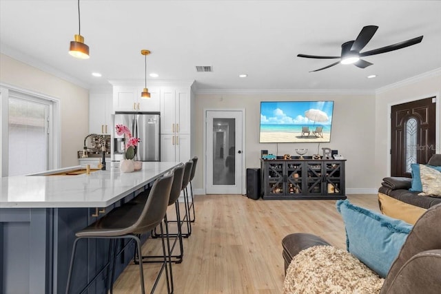 kitchen with decorative light fixtures, white cabinetry, stainless steel fridge, a kitchen bar, and ornamental molding