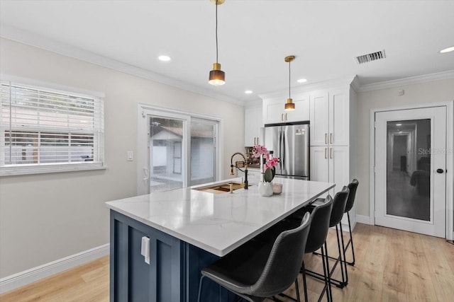 kitchen featuring sink, stainless steel fridge, light stone countertops, white cabinets, and decorative light fixtures