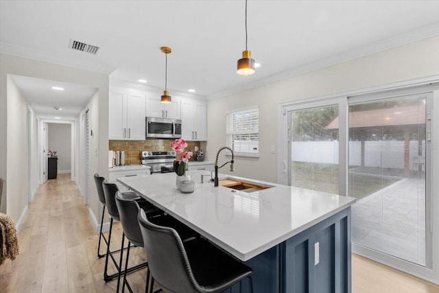 kitchen with pendant lighting, white cabinetry, stainless steel appliances, and a kitchen island with sink