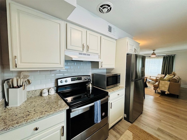 kitchen with appliances with stainless steel finishes, backsplash, light wood-type flooring, light stone countertops, and white cabinets