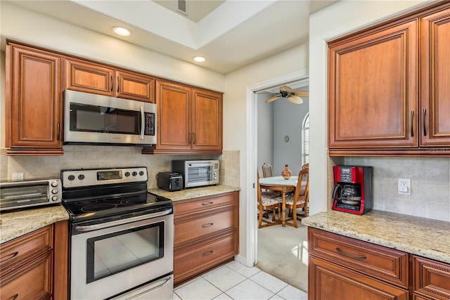 kitchen with stainless steel appliances, light stone countertops, light tile patterned floors, and backsplash