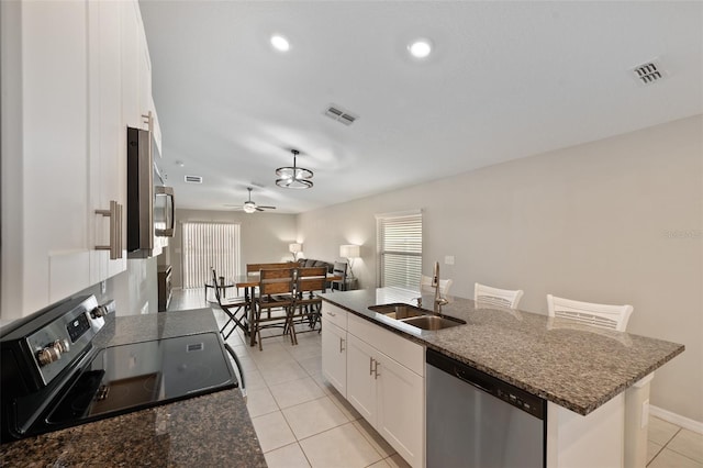 kitchen with light tile patterned flooring, white cabinetry, sink, stainless steel appliances, and a center island with sink