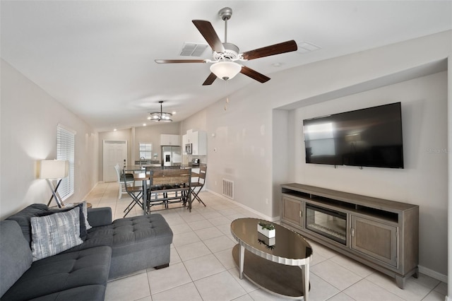 living room with lofted ceiling, light tile patterned floors, and ceiling fan with notable chandelier