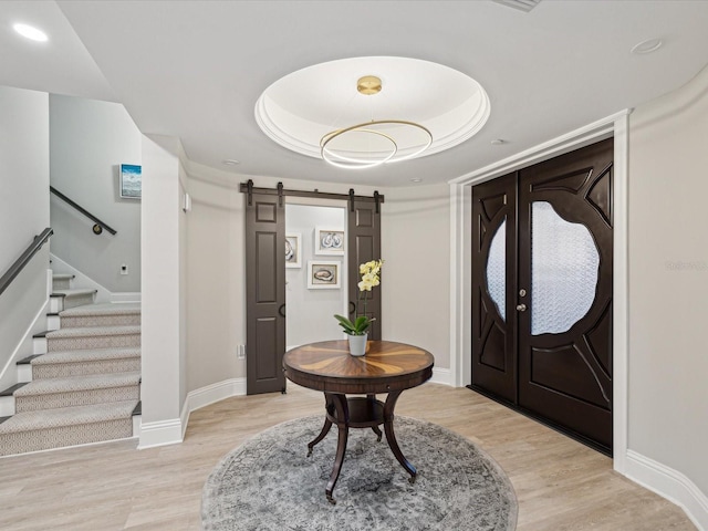 foyer featuring a tray ceiling, a barn door, and light hardwood / wood-style flooring