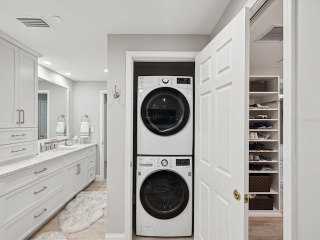 laundry room with sink, light hardwood / wood-style flooring, and stacked washer and clothes dryer