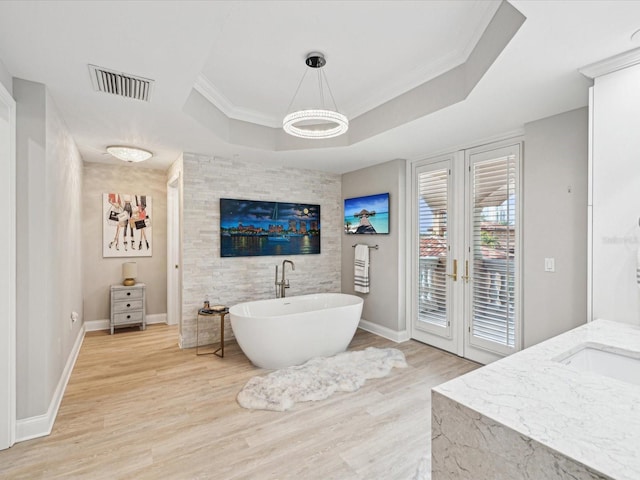 bathroom featuring hardwood / wood-style flooring, vanity, a bath, a tray ceiling, and ornamental molding